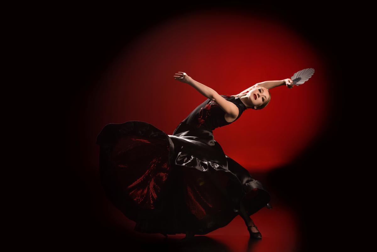 Una mujer joven bailando flamenco en un estudio profesional con un abanico en la mano.