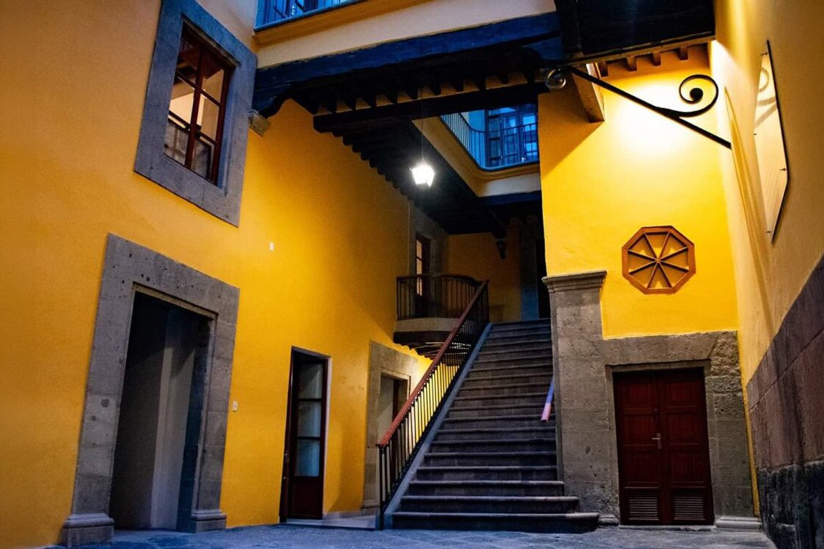 Interior courtyard of Casa de las campanas (bell house), a historic building with yellow walls, stone frames, wooden beams, and a central staircase.