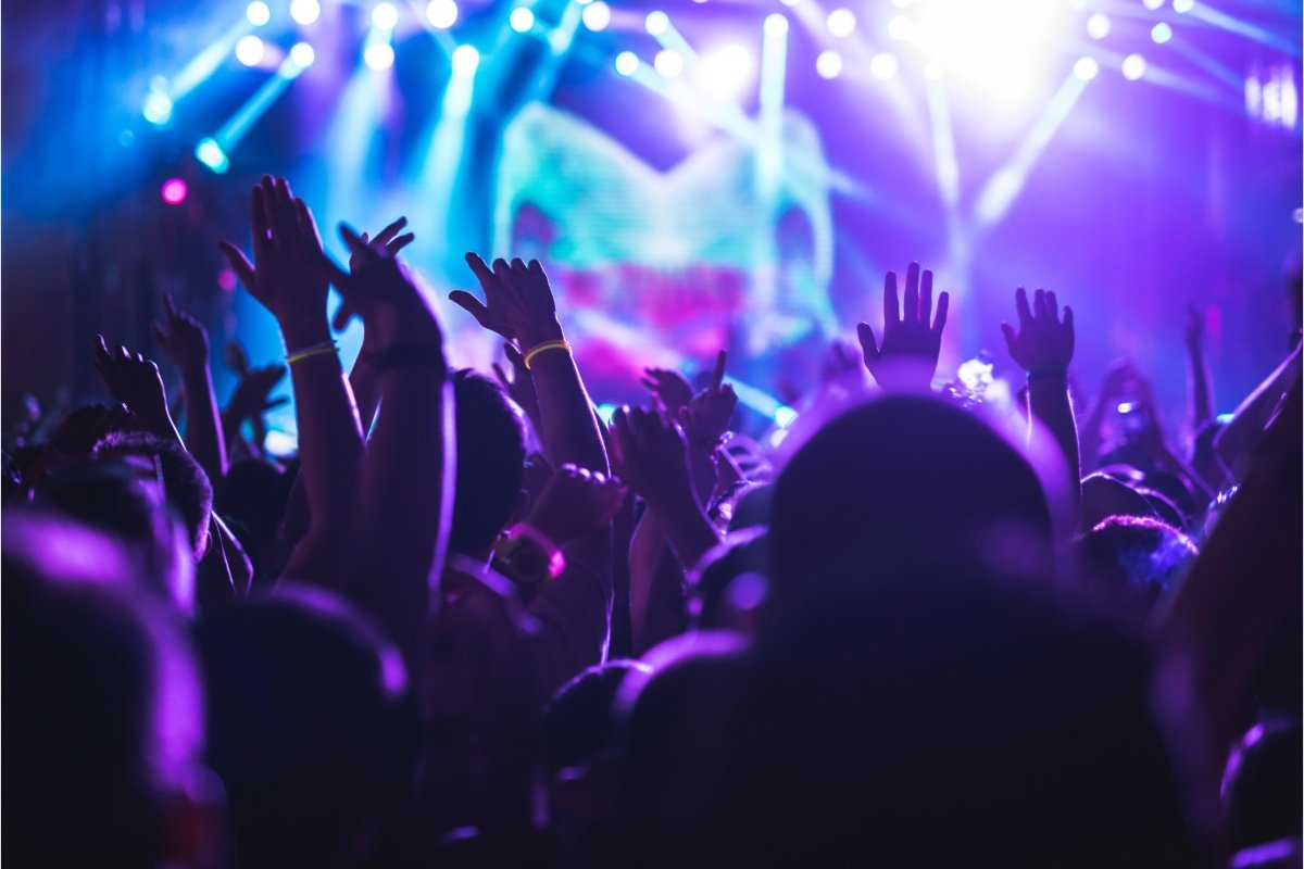 Concert crowd with hands raised, silhouetted against purple and blue stage lights