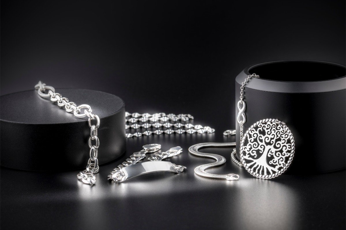 Tree-of-life pendant, chains, bracelets and an ID bracelet in silver arranged on black cylindrical display stands