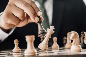 A hand using a black piece to topple the white king on a chessboard