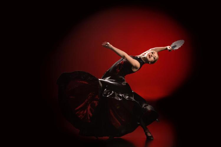 Una mujer joven bailando flamenco en un estudio profesional con un abanico en la mano.
