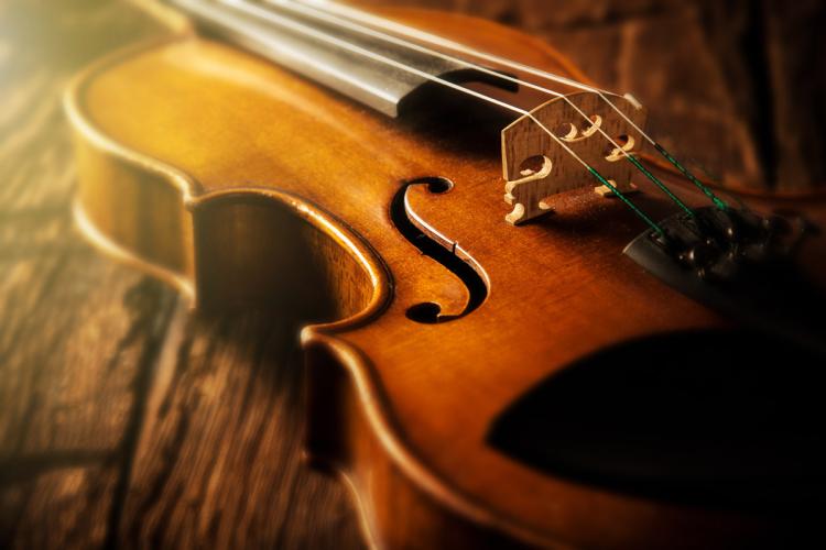Violín de madera sobre una superficie de madera, iluminado cálidamente. Se destacan las cuerdas y la curvatura del puente.