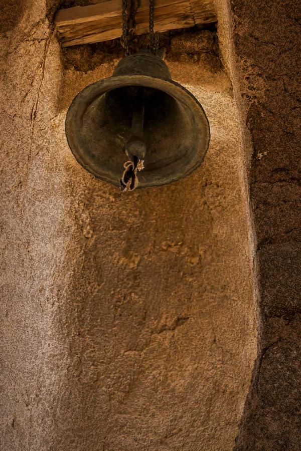 Antique bronze bell suspended by chains in a rustic, textured stone niche.